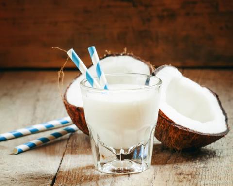 Coconut milk in a glass with striped straw and coconut halves, selective focus