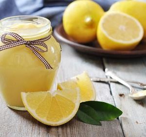 Lemon curd in glass jar with fresh lemons on wooden background
