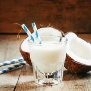 Coconut milk in a glass with striped straw and coconut halves, selective focus